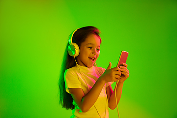 Image showing Portrait of little girl in headphones on green background in neon light