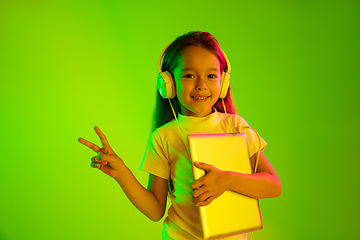 Image showing Portrait of little girl in headphones on green background in neon light