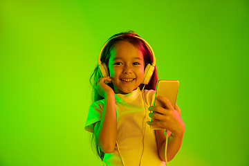 Image showing Portrait of little girl in headphones on green background in neon light