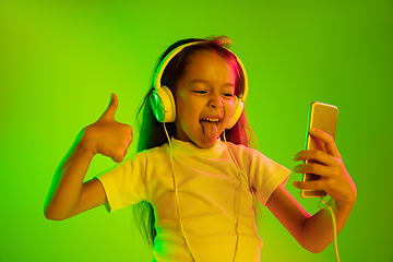 Image showing Portrait of little girl in headphones on green background in neon light