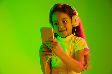 Image showing Portrait of little girl in headphones on green background in neon light