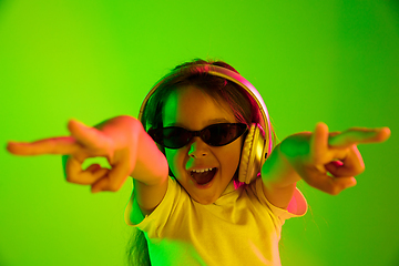 Image showing Portrait of little girl in headphones on green background in neon light