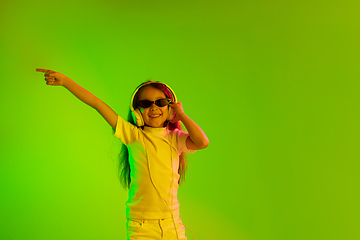 Image showing Portrait of little girl in headphones on green background in neon light