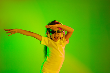 Image showing Portrait of little girl in headphones on green background in neon light