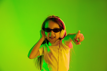 Image showing Portrait of little girl in headphones on green background in neon light