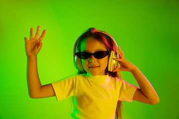 Image showing Portrait of little girl in headphones on green background in neon light