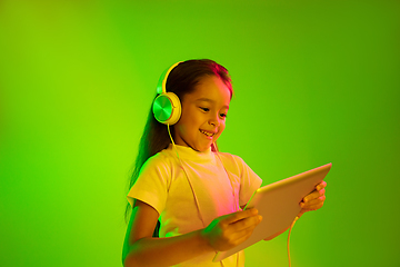 Image showing Portrait of little girl in headphones on green background in neon light