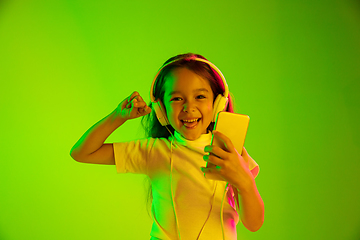 Image showing Portrait of little girl in headphones on green background in neon light