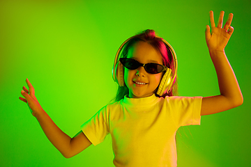 Image showing Portrait of little girl in headphones on green background in neon light