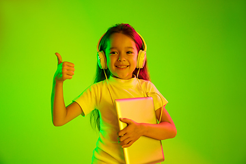 Image showing Portrait of little girl in headphones on green background in neon light