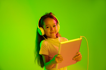 Image showing Portrait of little girl in headphones on green background in neon light