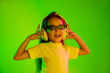 Image showing Portrait of little girl in headphones on green background in neon light