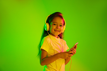 Image showing Portrait of little girl in headphones on green background in neon light