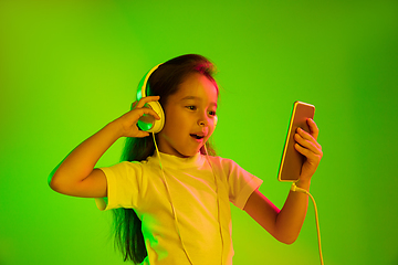 Image showing Portrait of little girl in headphones on green background in neon light