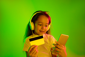 Image showing Portrait of little girl in headphones on green background in neon light