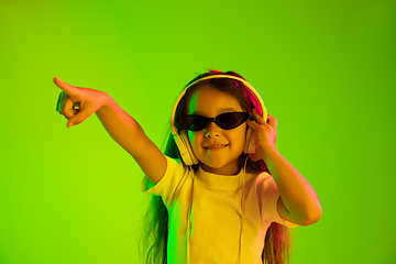 Image showing Portrait of little girl in headphones on green background in neon light