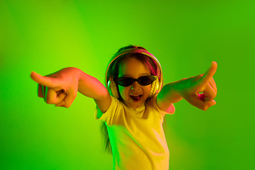 Image showing Portrait of little girl in headphones on green background in neon light