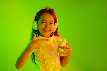 Image showing Portrait of little girl in headphones on green background in neon light