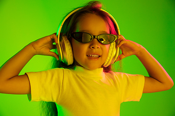 Image showing Portrait of little girl in headphones on green background in neon light