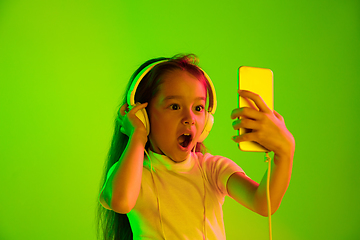 Image showing Portrait of little girl in headphones on green background in neon light