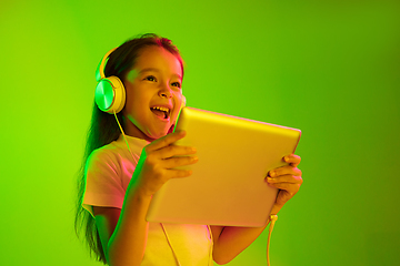 Image showing Portrait of little girl in headphones on green background in neon light