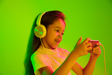 Image showing Portrait of little girl in headphones on green background in neon light