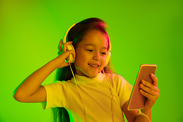 Image showing Portrait of little girl in headphones on green background in neon light