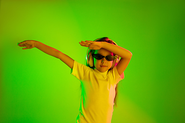 Image showing Portrait of little girl in headphones on green background in neon light