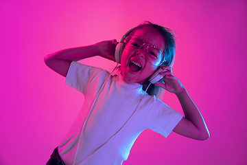 Image showing Portrait of little girl in headphones on purple gradient background in neon light