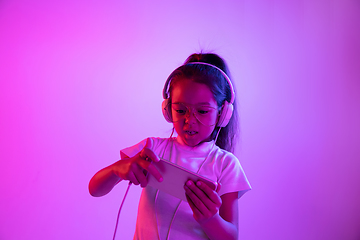 Image showing Portrait of little girl in headphones on purple gradient background in neon light