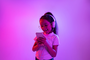 Image showing Portrait of little girl in headphones on purple gradient background in neon light