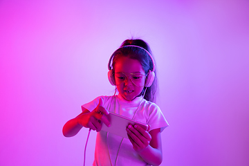 Image showing Portrait of little girl in headphones on purple gradient background in neon light