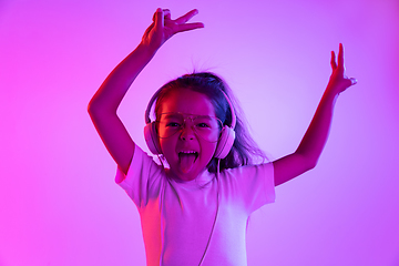 Image showing Portrait of little girl in headphones on purple gradient background in neon light