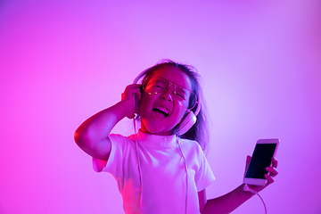 Image showing Portrait of little girl in headphones on purple gradient background in neon light