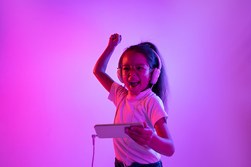 Image showing Portrait of little girl in headphones on purple gradient background in neon light