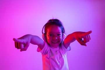 Image showing Portrait of little girl in headphones on purple gradient background in neon light