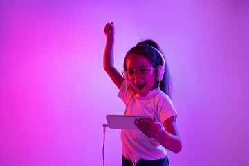 Image showing Portrait of little girl in headphones on purple gradient background in neon light