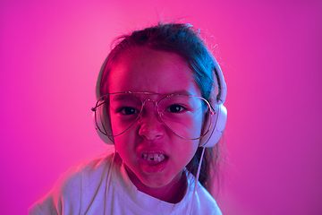 Image showing Portrait of little girl in headphones on purple gradient background in neon light