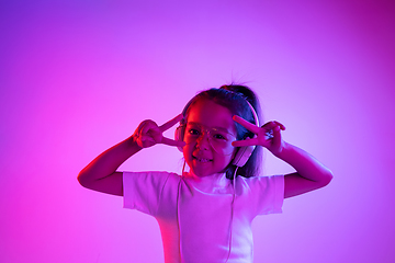 Image showing Portrait of little girl in headphones on purple gradient background in neon light