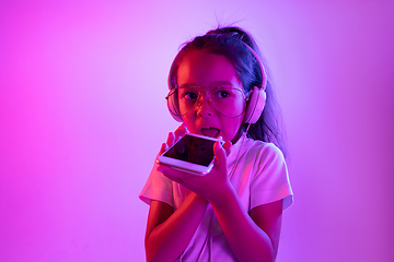 Image showing Portrait of little girl in headphones on purple gradient background in neon light