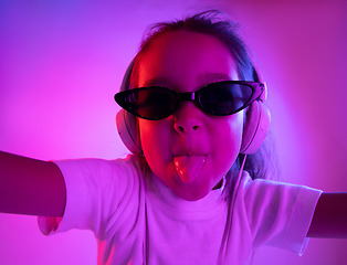 Image showing Portrait of little girl in headphones on purple gradient background in neon light