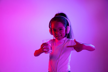 Image showing Portrait of little girl in headphones on purple gradient background in neon light