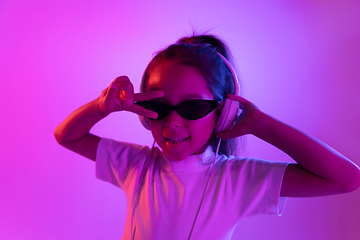 Image showing Portrait of little girl in headphones on purple gradient background in neon light