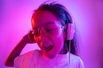 Image showing Portrait of little girl in headphones on purple gradient background in neon light