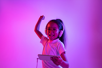 Image showing Portrait of little girl in headphones on purple gradient background in neon light