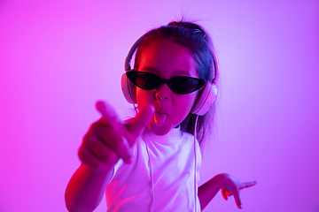 Image showing Portrait of little girl in headphones on purple gradient background in neon light