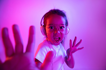 Image showing Portrait of little girl in headphones on purple gradient background in neon light