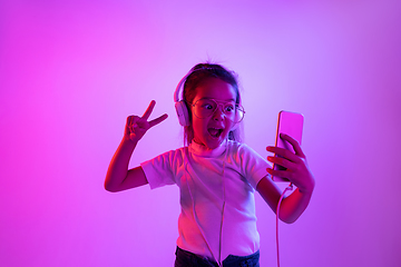 Image showing Portrait of little girl in headphones on purple gradient background in neon light