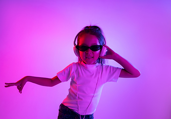 Image showing Portrait of little girl in headphones on purple gradient background in neon light