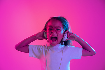 Image showing Portrait of little girl in headphones on purple gradient background in neon light